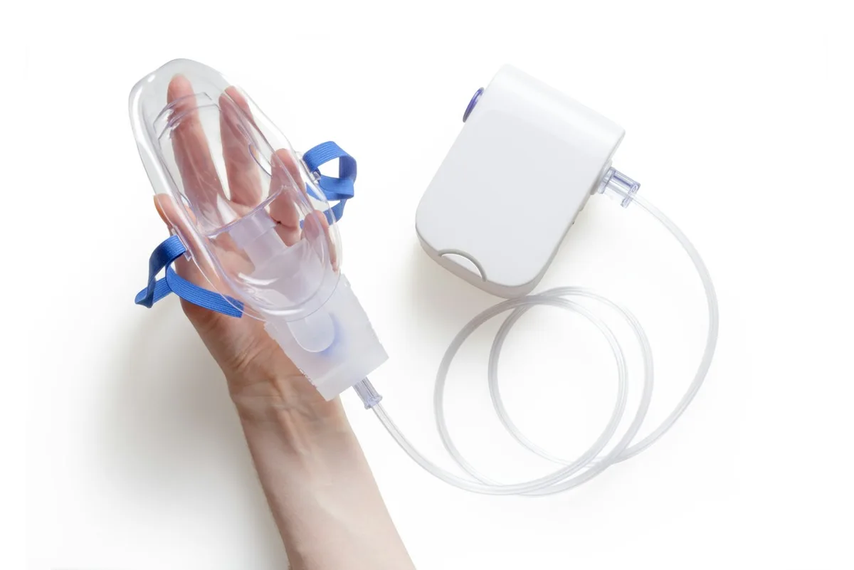 Máscara de nebulização transparente ao lado de um aparelho branco