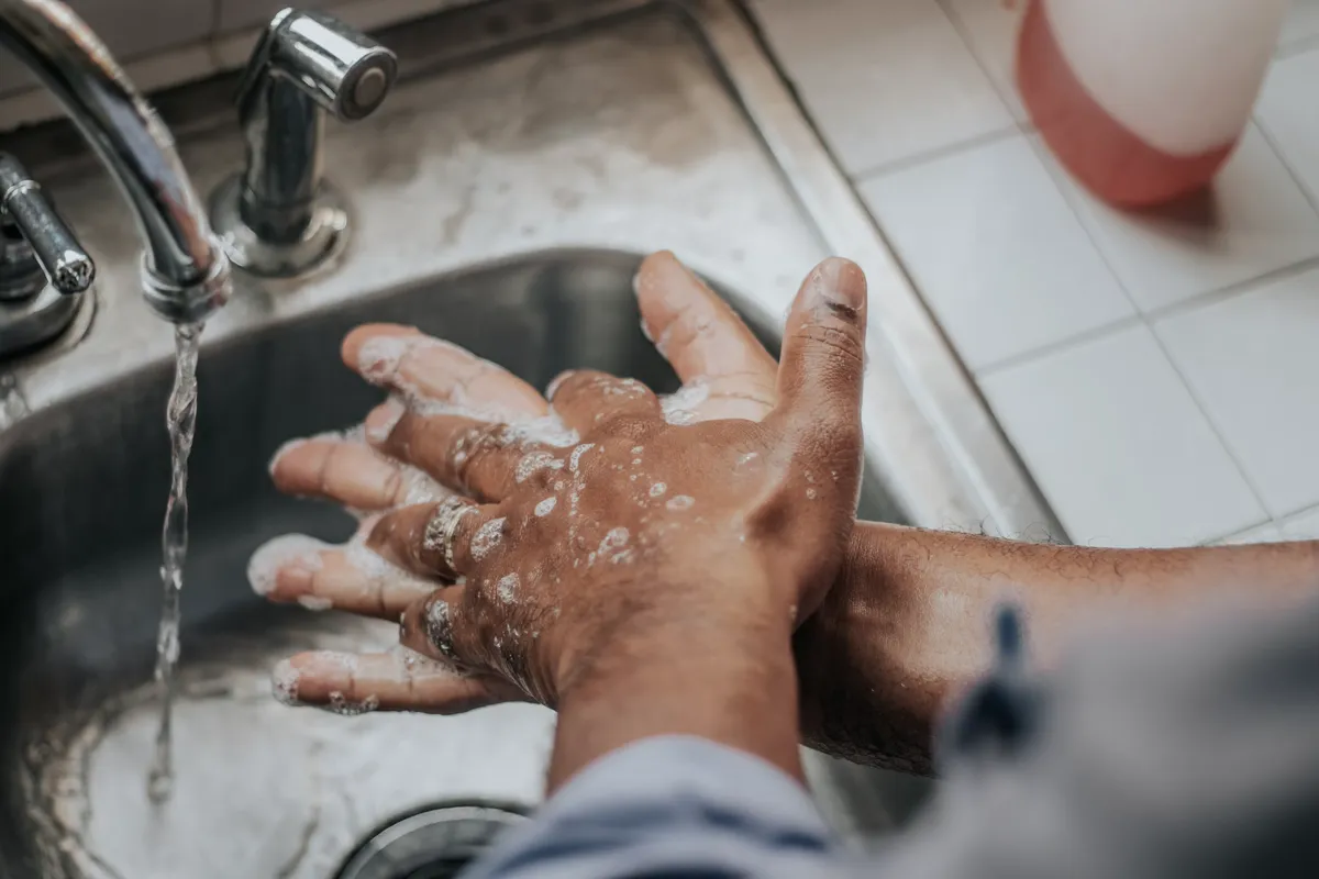 Mãos cobertas de espuma sendo esfregadas sob a água da torneira